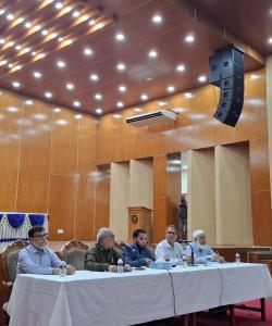 Presentors behind white tableclothed table and moderator at stand