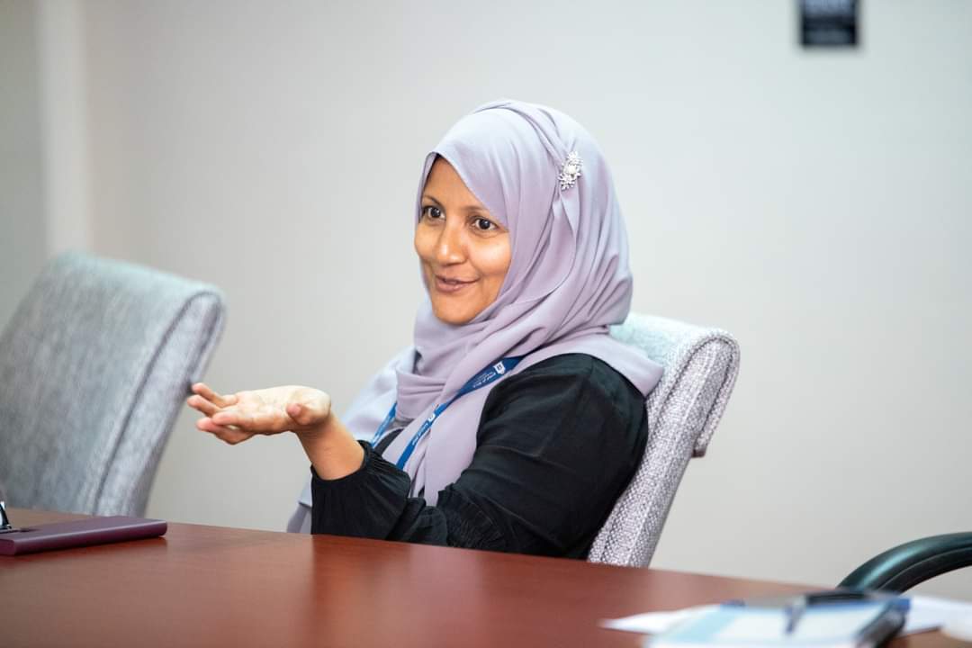 Lady in lilac hijab accross table speaking and smiling